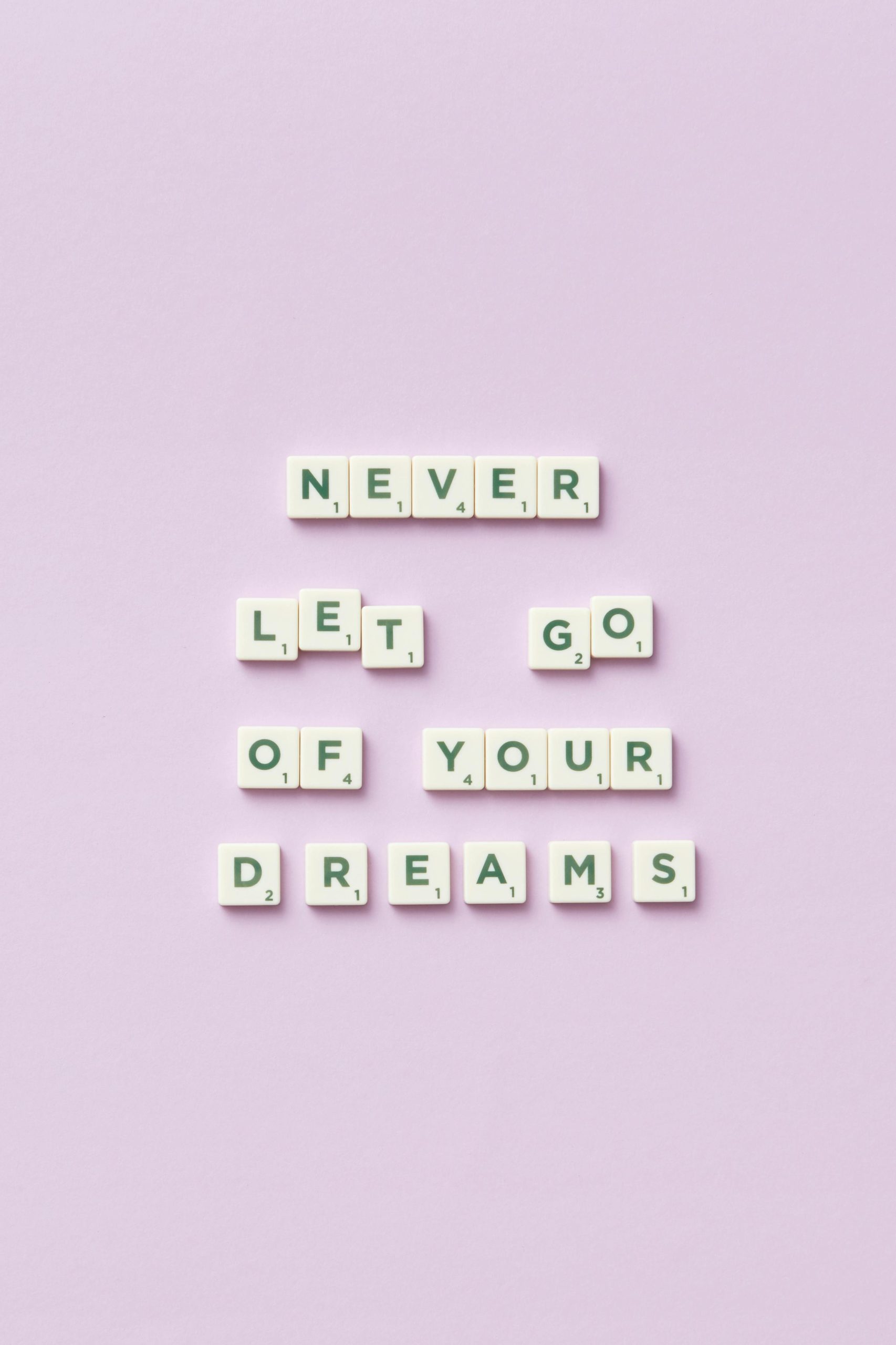 Letter tiles épellent « Never let go of your dreams » sur un fond pastel violet.