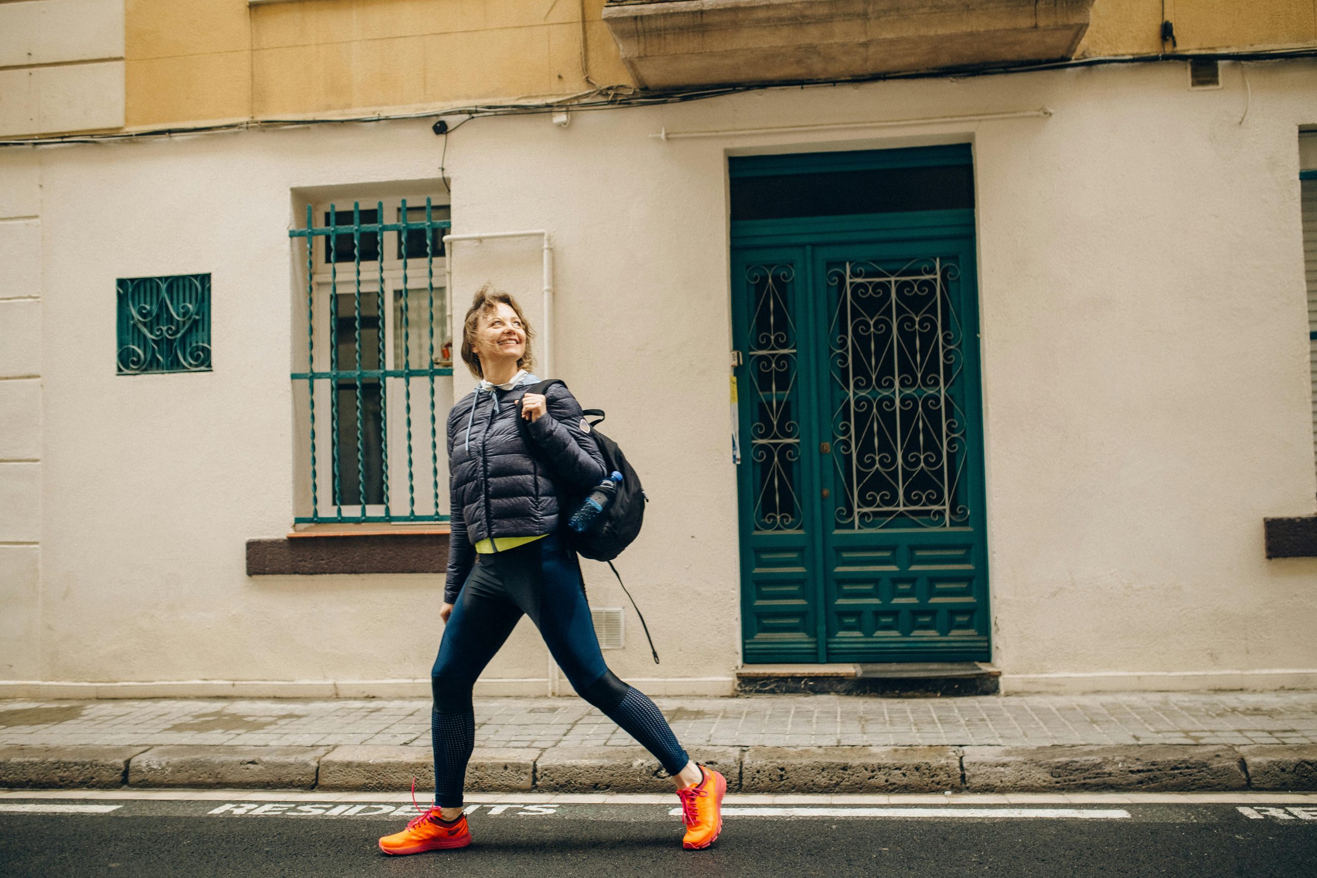 Une femme souriante en tenue de sport marche avec énergie dans une rue ensoleillée, illustrant un mode de vie urbain.