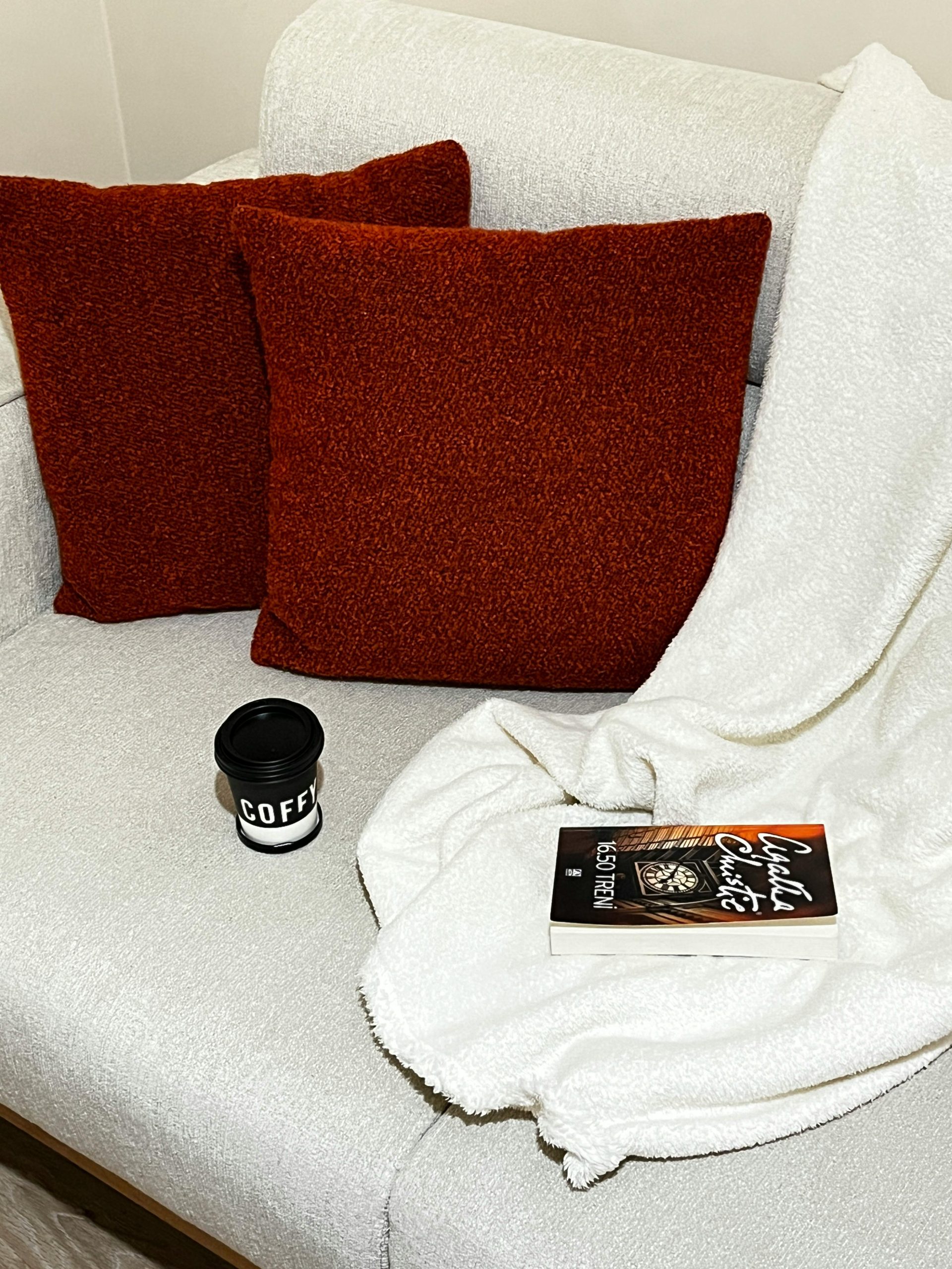 Un coin lecture paisible avec des coussins, un livre et du café sur un canapé confortable.