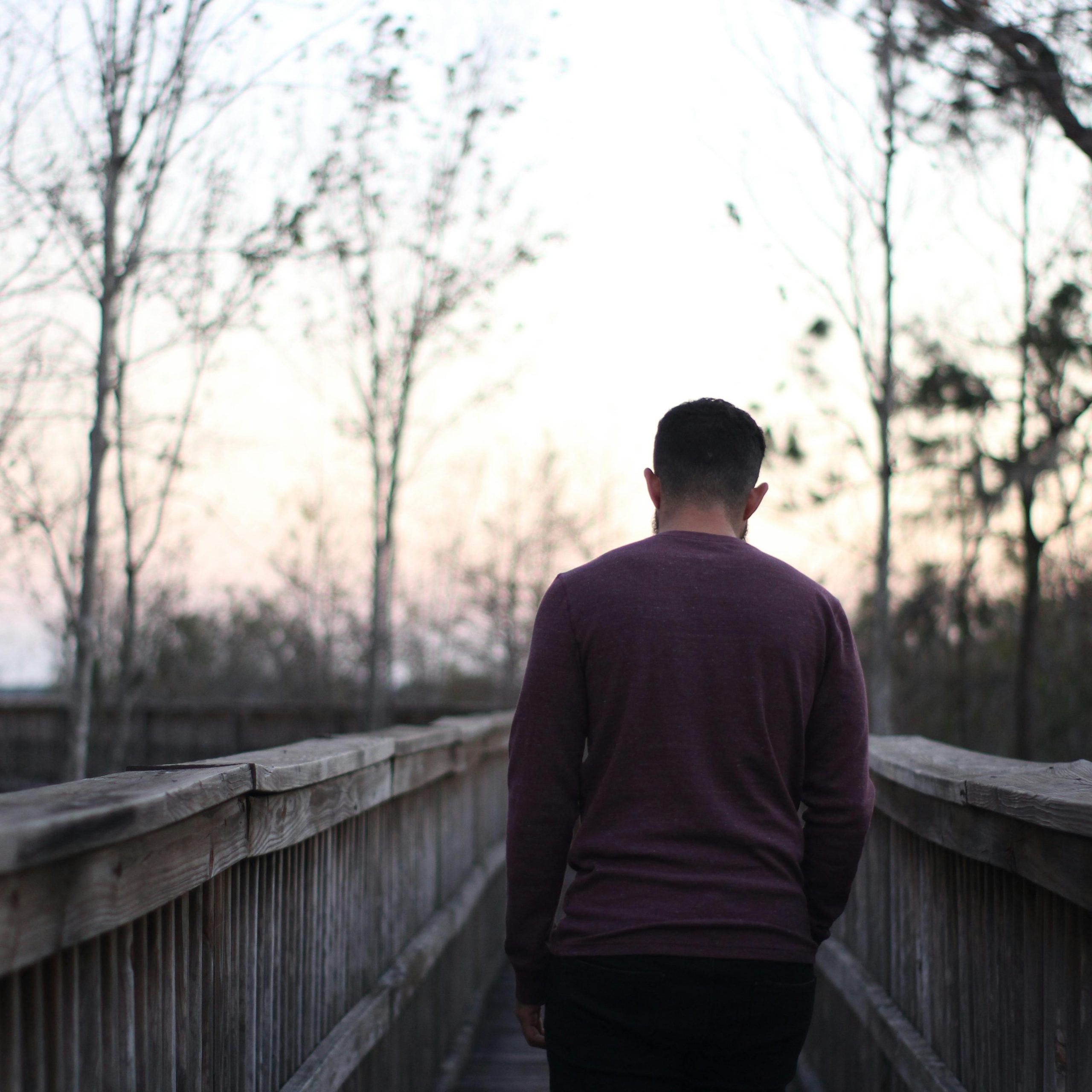 Un homme marche le long d'un pont en bois dans un cadre crépusculaire serein, illustrant la tranquillité et la solitude.