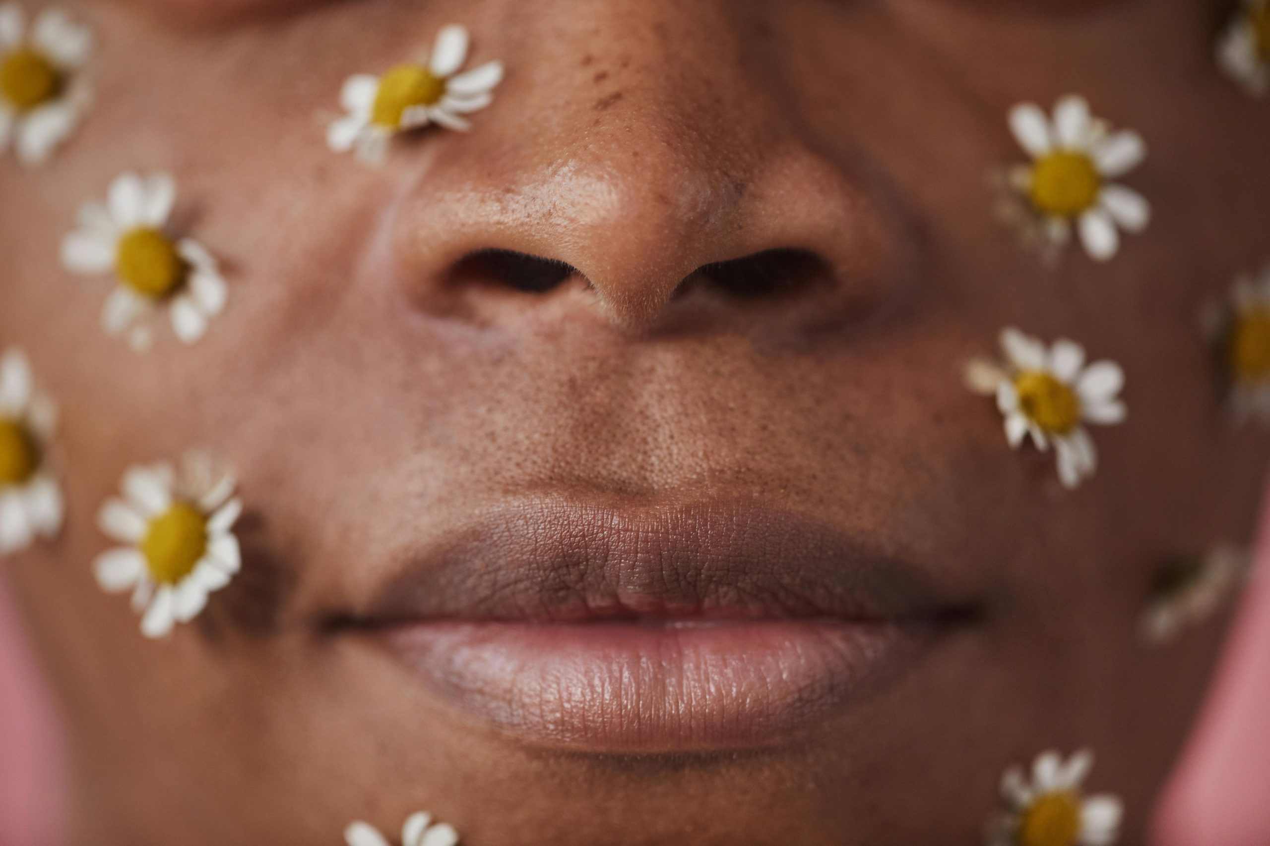 An artistic face close-up adorned with white flowers on a warm-toned skin backdrop. Visage artistique en gros plan orné de fleurs blanches sur un fond de peau aux tons chauds.